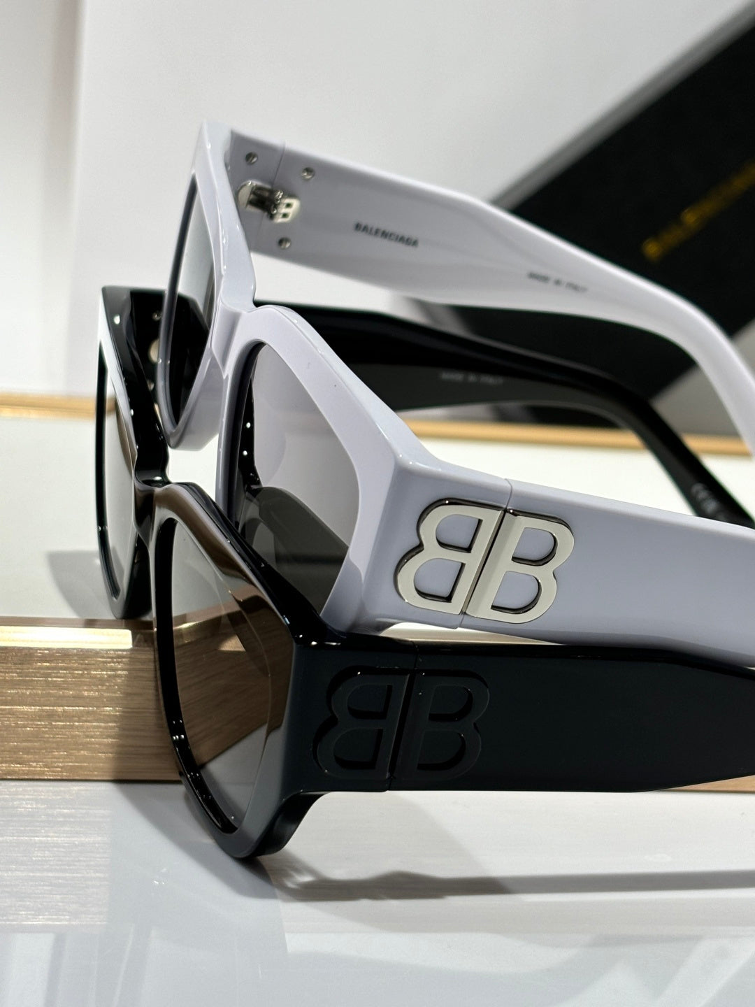 Balenciaga sunglasses side view with white frames, dark lenses, and gold B B logo.