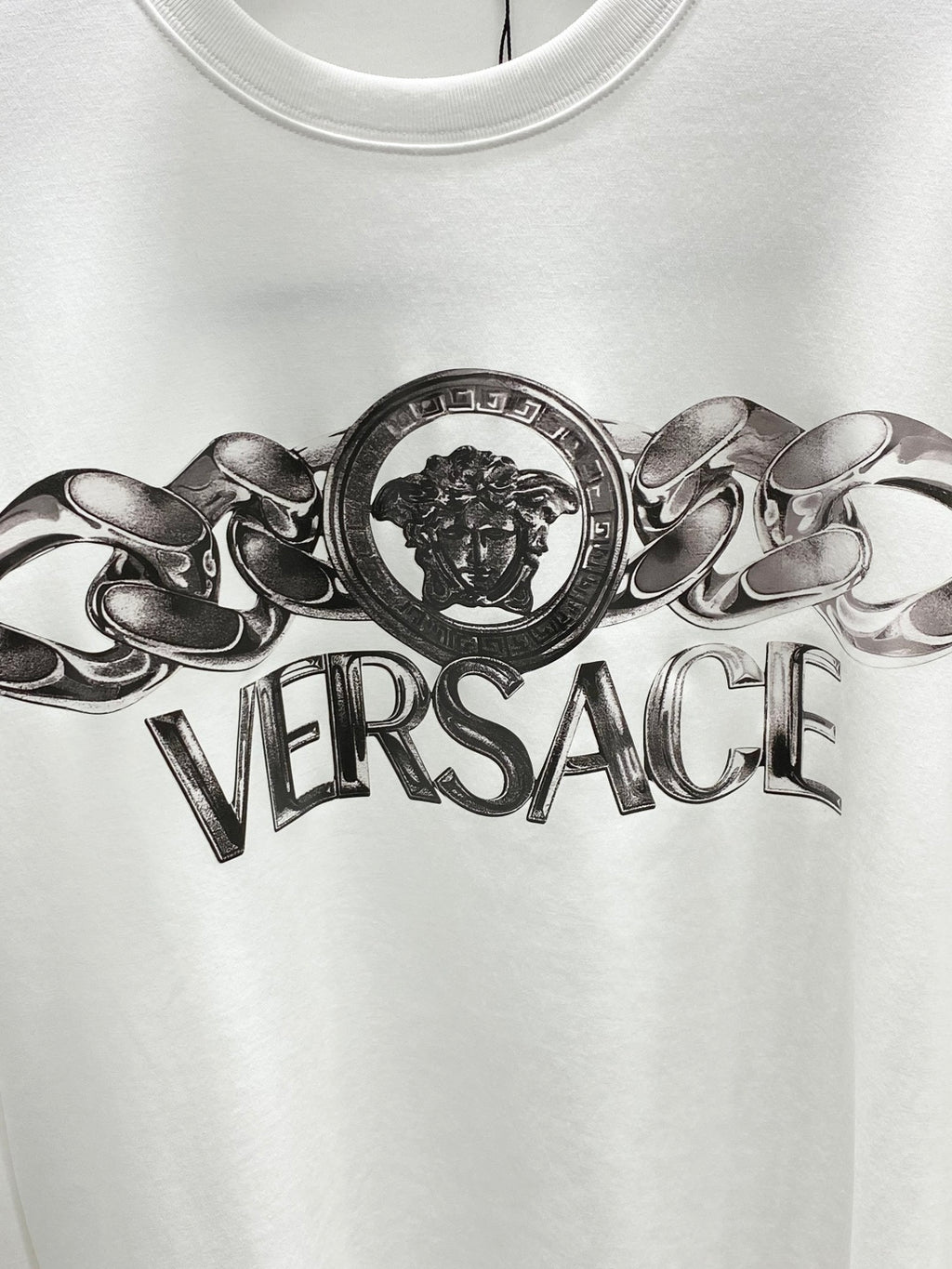 Versace white crewneck T-shirt close-up of metallic lion crest and Versace text