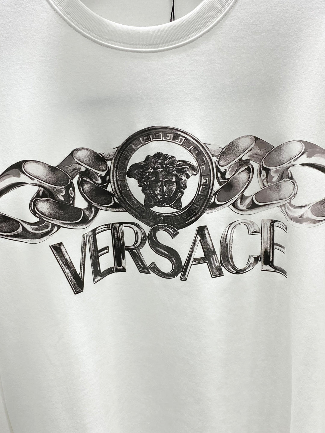 Versace white crewneck T-shirt close-up of metallic lion crest and Versace text