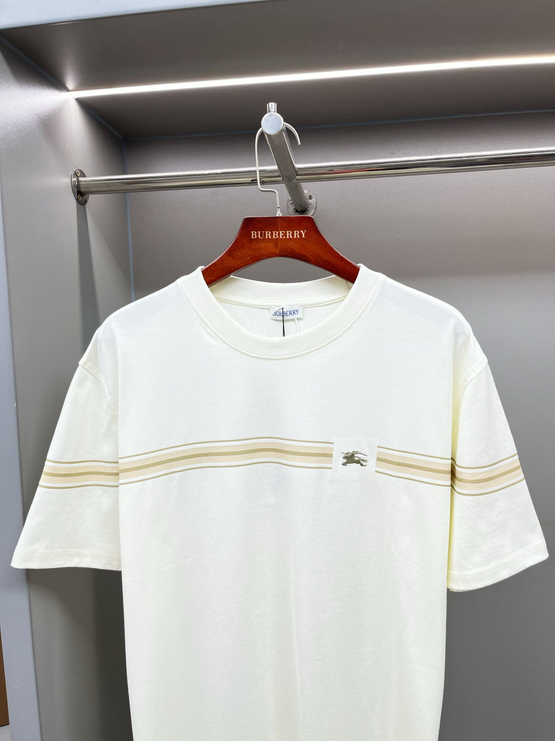 White Burberry T-shirt with gold stripe band across chest, on hanger