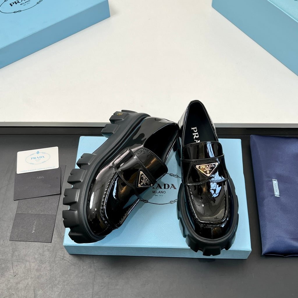 Black patent loafers with thick lug soles, showing side strap buckle details