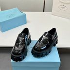 Black platform loafers with glossy finish, strap buckle, and thick lug sole