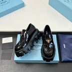 Two black patent loafers on blue box, showing strap buckle and lug platform soles