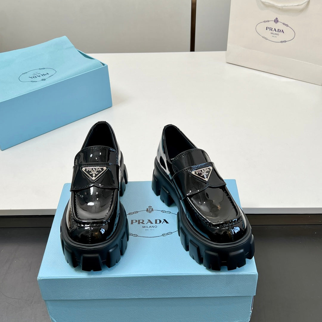 Pair of black patent loafers with strap buckle and chunky treaded sole