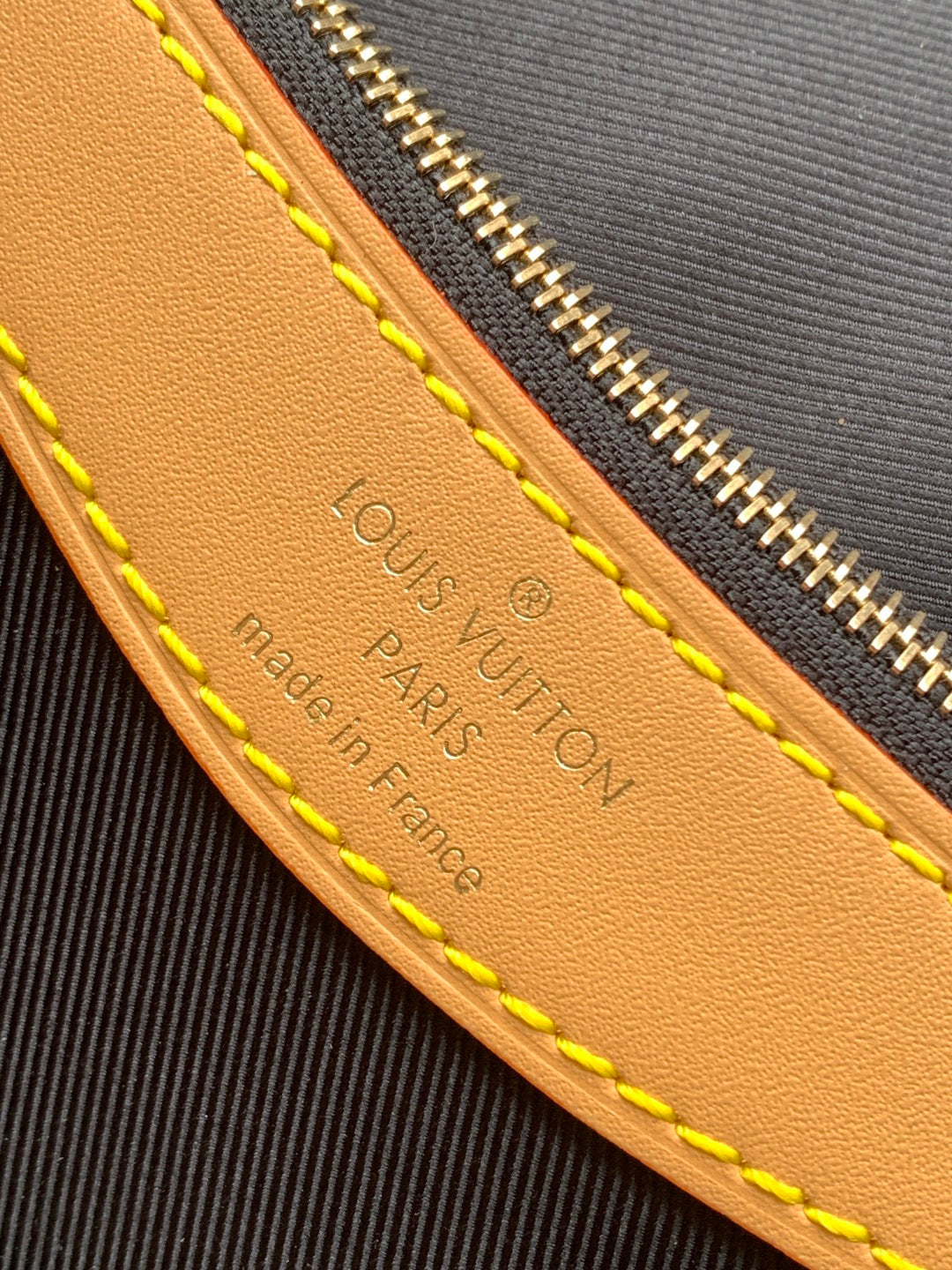 Embossed leather panel with text and yellow edge stitching on monogram canvas