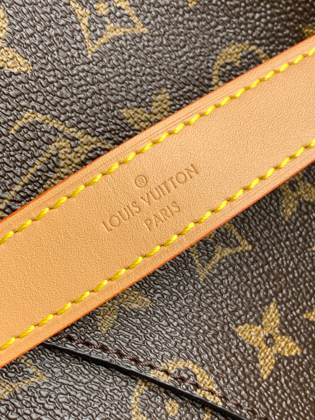 Tan leather strap detail with embossed text and yellow edge stitching