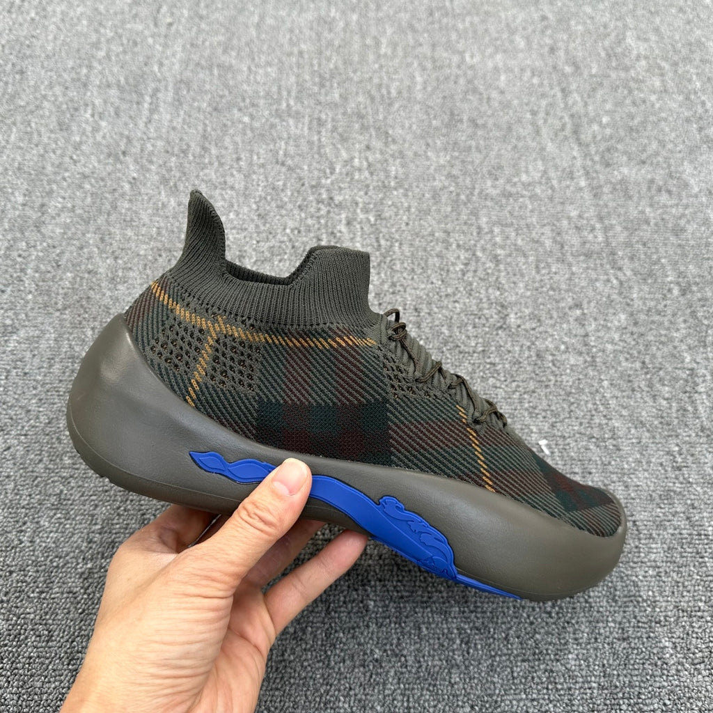 Plaid knit sneaker held in hand, with blue stripe on the side sole edge