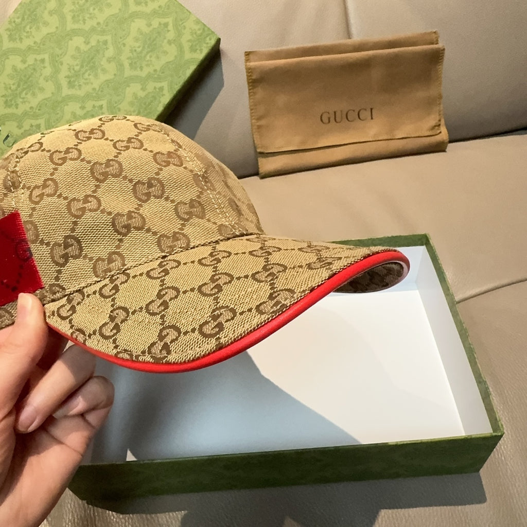 Gucci baseball cap with GG monogram fabric and red-edged brim, held in hand.