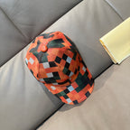Plaid baseball cap in orange, green, black, and white with button on crown