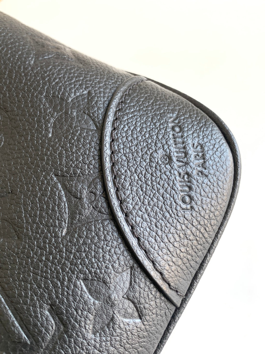 Louis Vuitton black leather bag corner close-up with embossed logo on flap