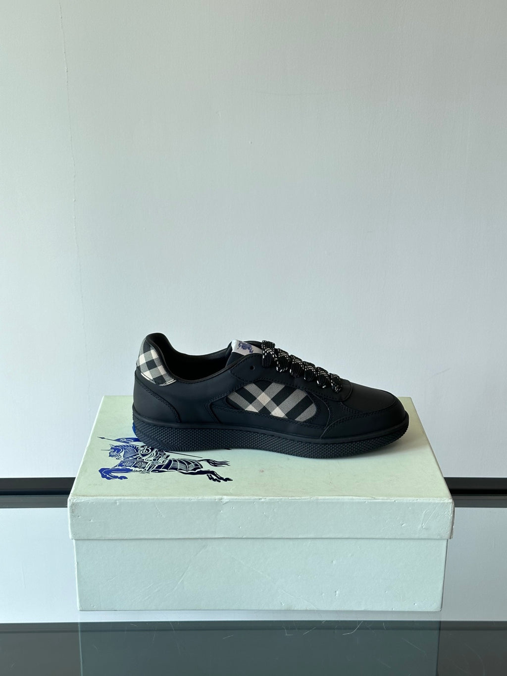 Black low-top sneaker on a box with plaid panel and black textured lace-up