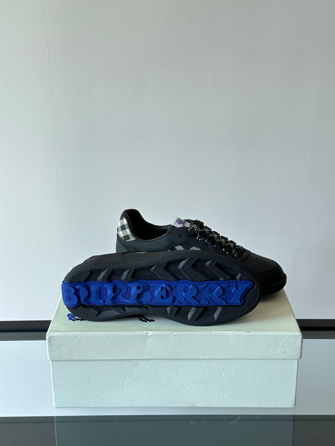 Single black low-top sneaker on a box with blue logo accent and plaid panel