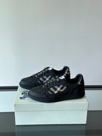 Black low-top sneakers with plaid strap detail and textured lace-up closure