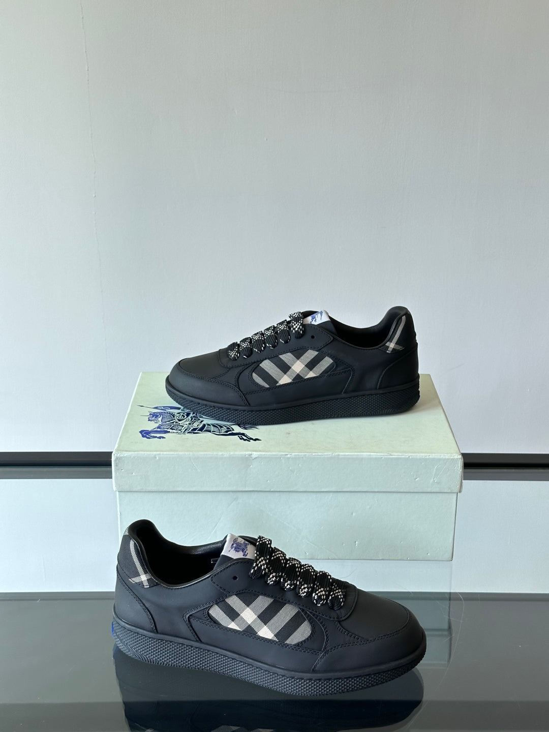 Two black low-top sneakers on a box, plaid accents and black textured laces