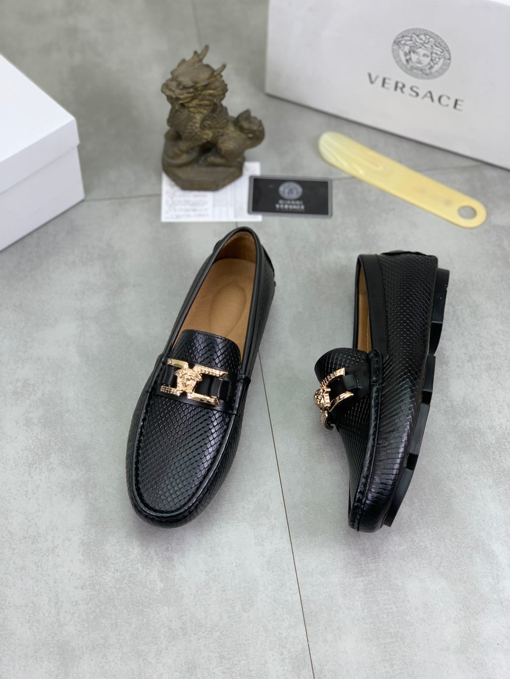 Black leather loafers, one front and one side view, gold-tone buckle detail
