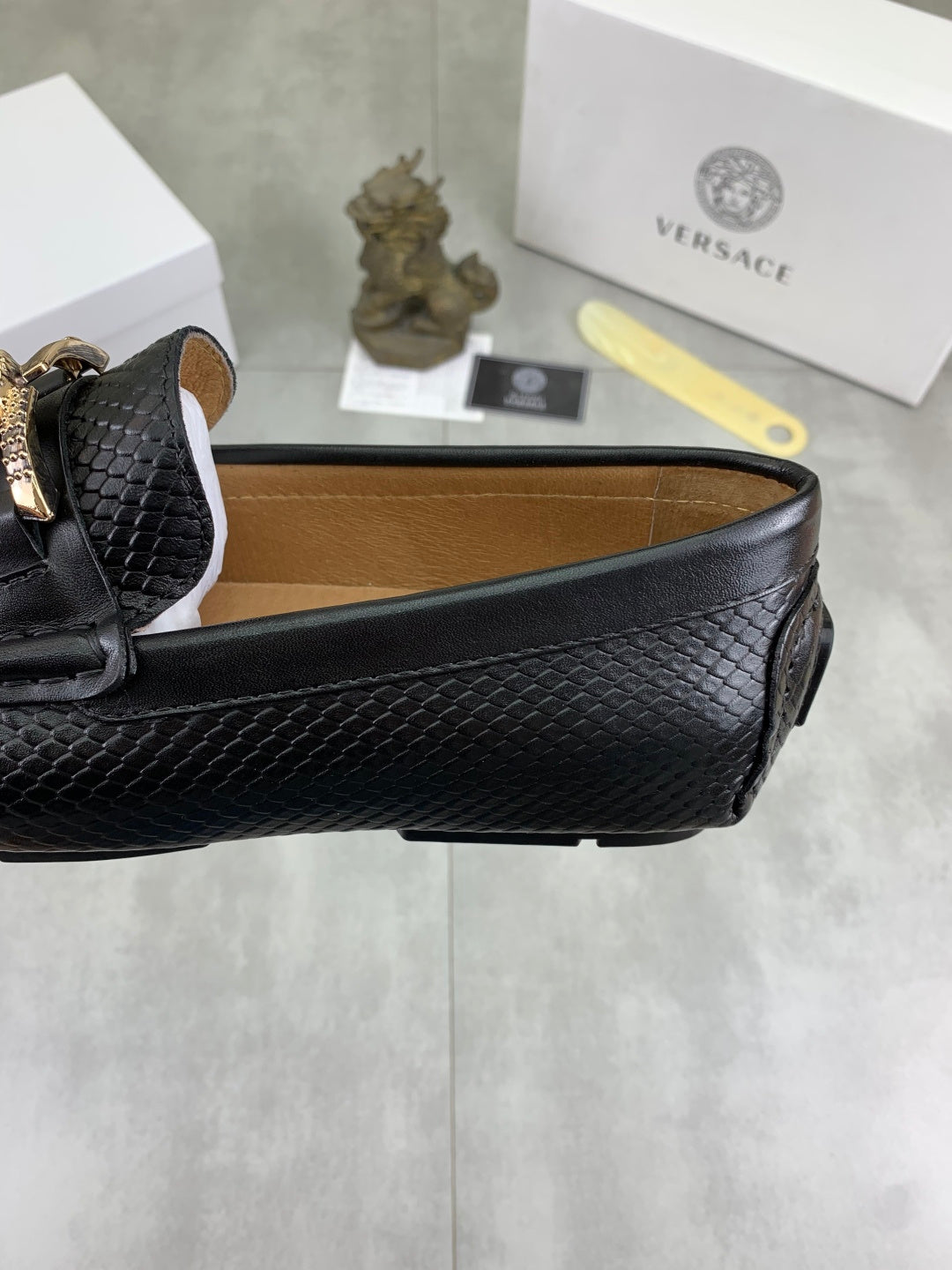 Black leather loafer showing side panel and gold-tone buckle, close angle