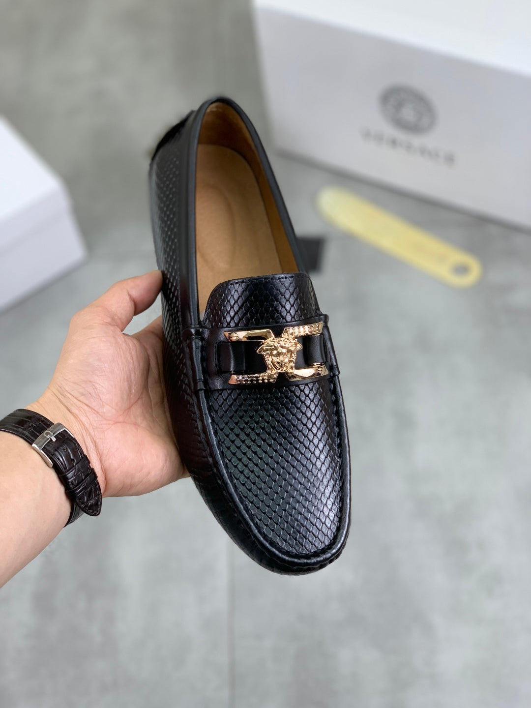Black leather loafer with gold-tone buckle detail, hand-held front view