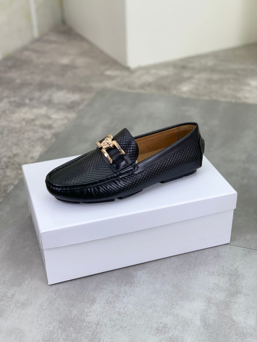 Black leather loafer with gold-tone buckle strap and low-profile sole, side view