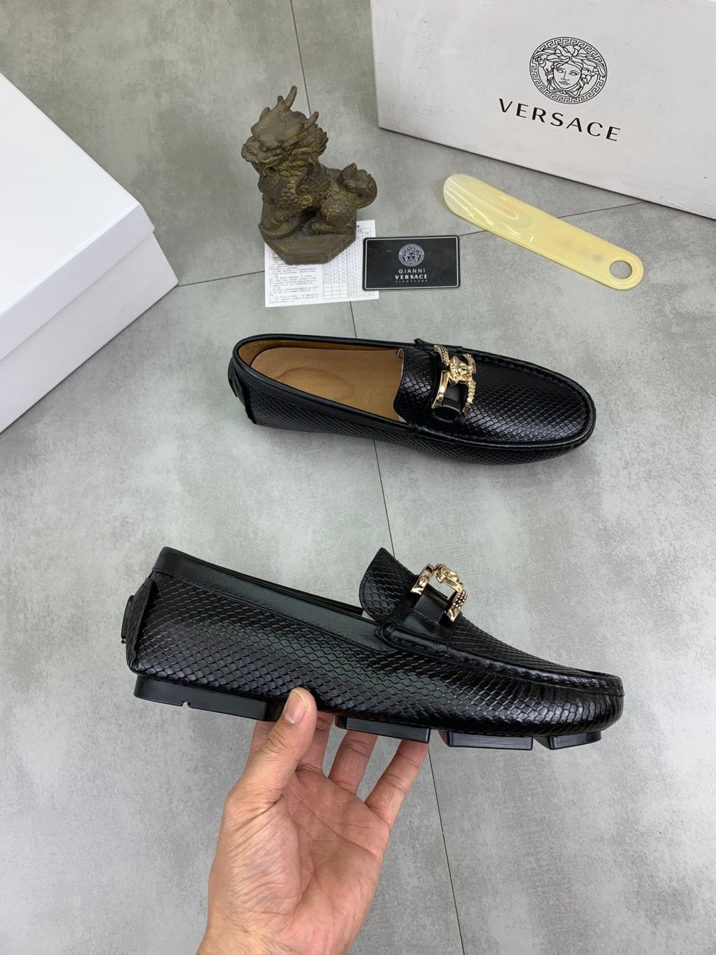 Black leather loafer with gold-tone buckle strap, held side and top view