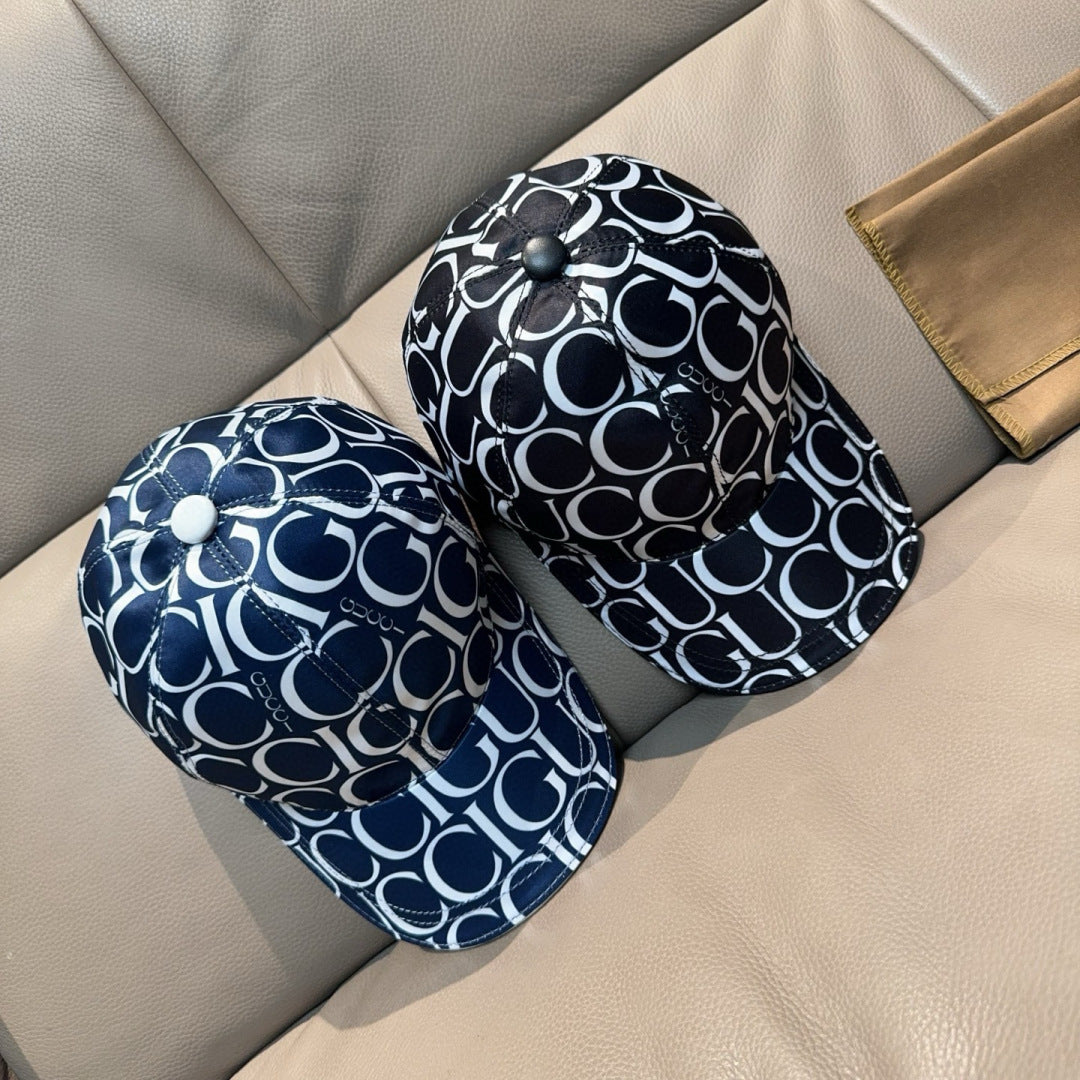 Pair of Gucci caps in navy with white GG monogram pattern, curved brims side by side.