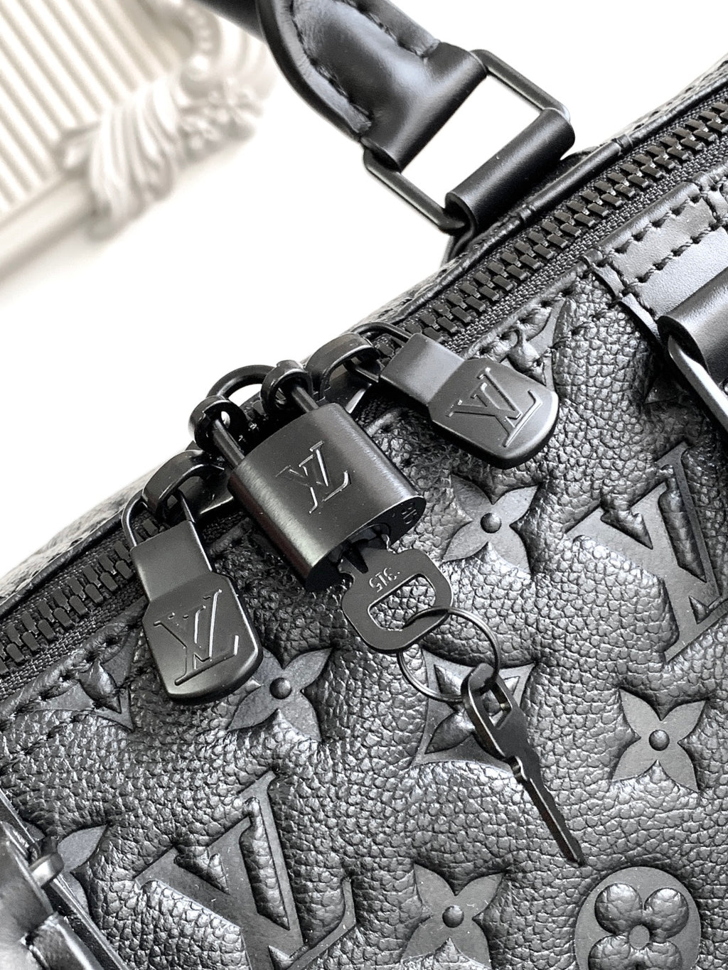 Black monogram duffel bag zipper pulls with metal charms and embossed pattern