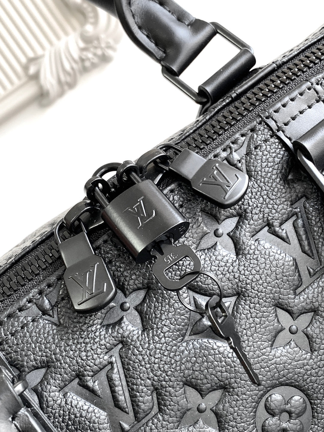 Black monogram duffel bag zipper pulls with metal charms and embossed pattern