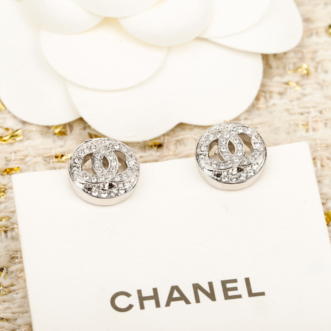 Silver CHANEL logo stud earrings on a white display card