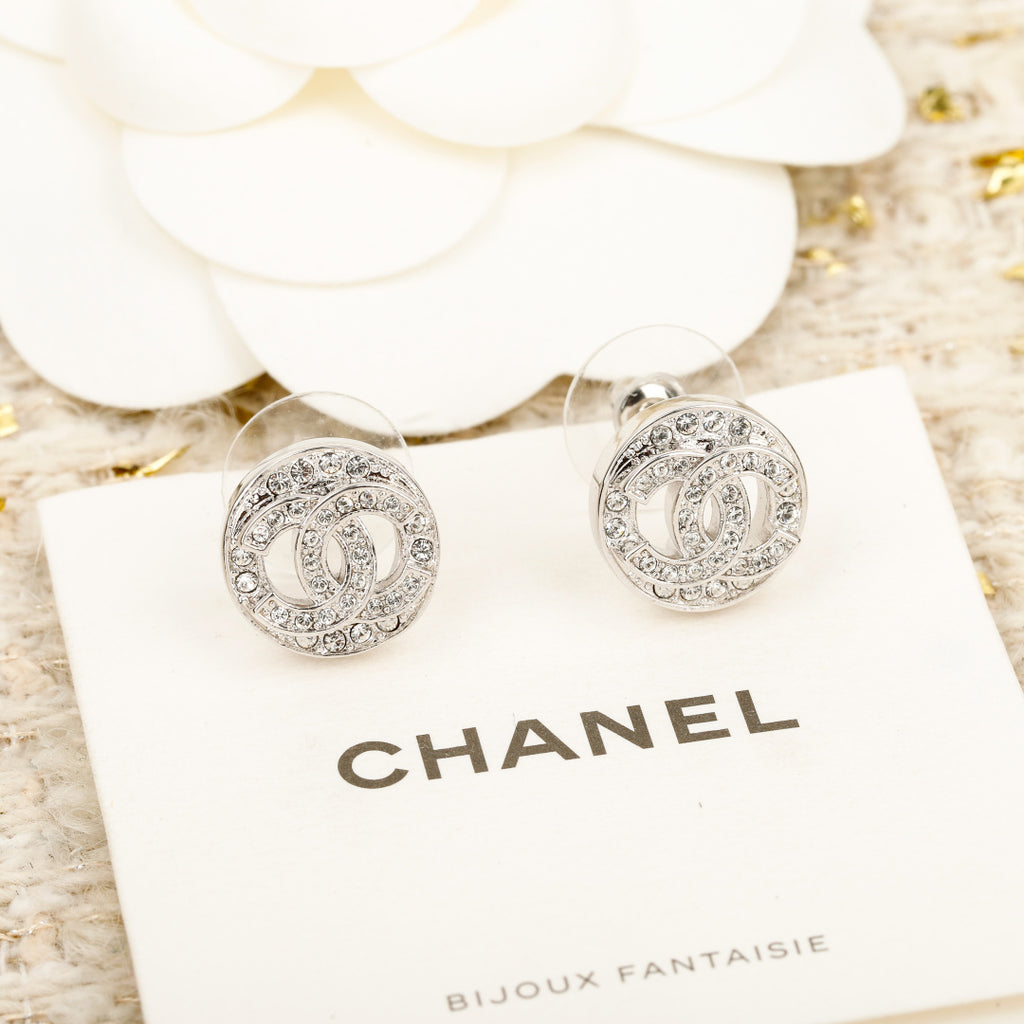 Silver CHANEL logo stud earrings on a branded display card