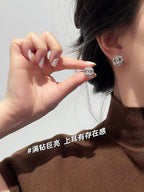 CHANEL logo stud earrings worn on an ear, with hands adjusting the jewelry
