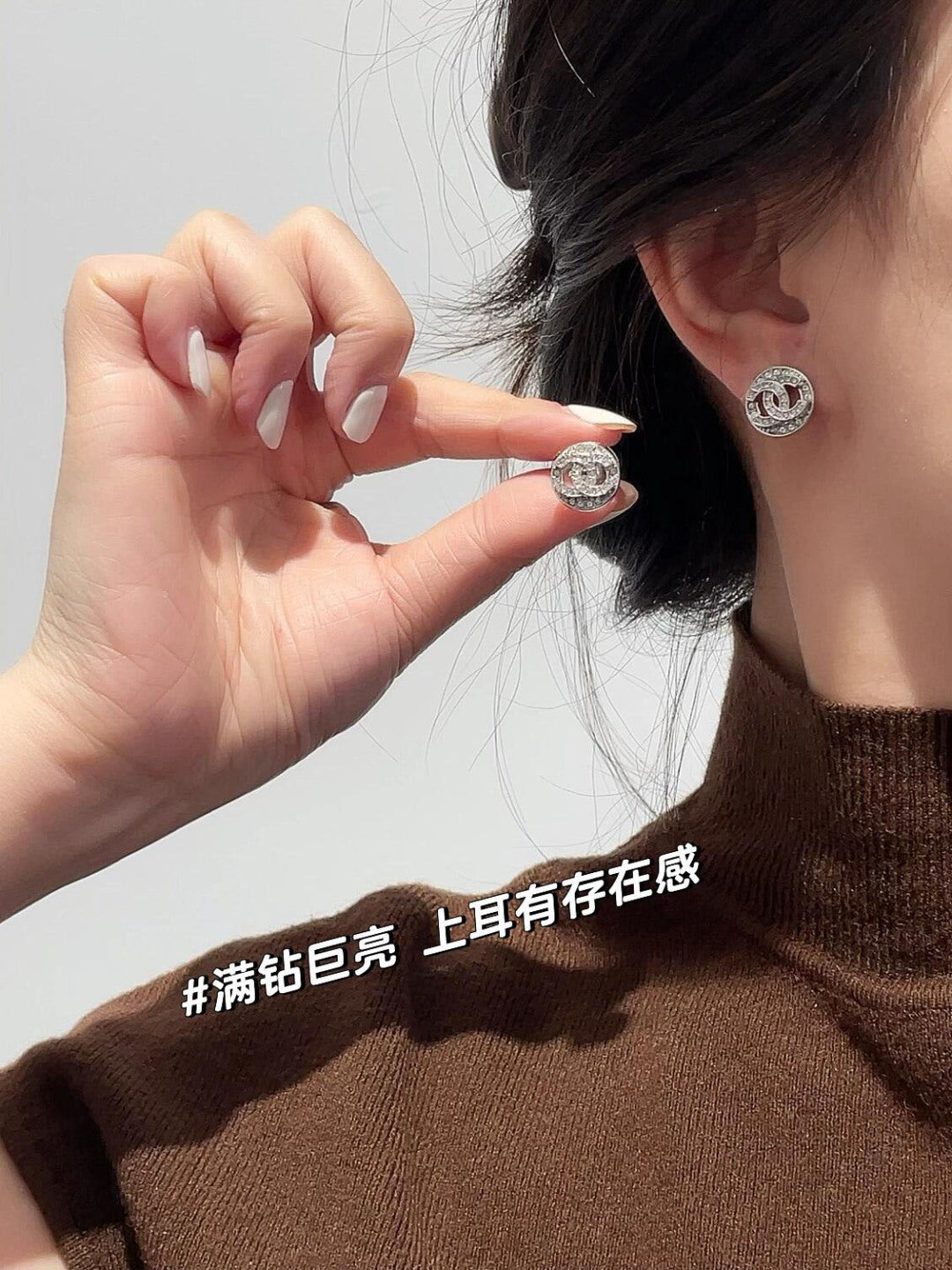 CHANEL logo stud earrings worn on an ear, with hands adjusting the jewelry