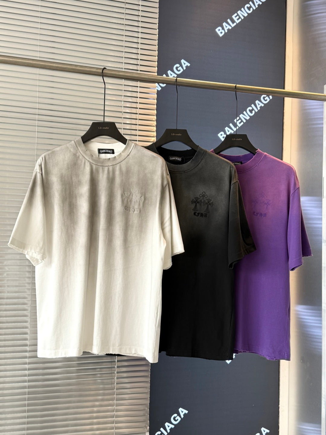 Short-sleeve T-shirts in white, dark gray, and purple with embroidered chest graphics.