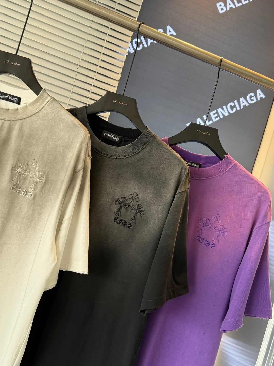 Short-sleeve T-shirts on hangers: cream, dark gray, and purple with small embroidered art.