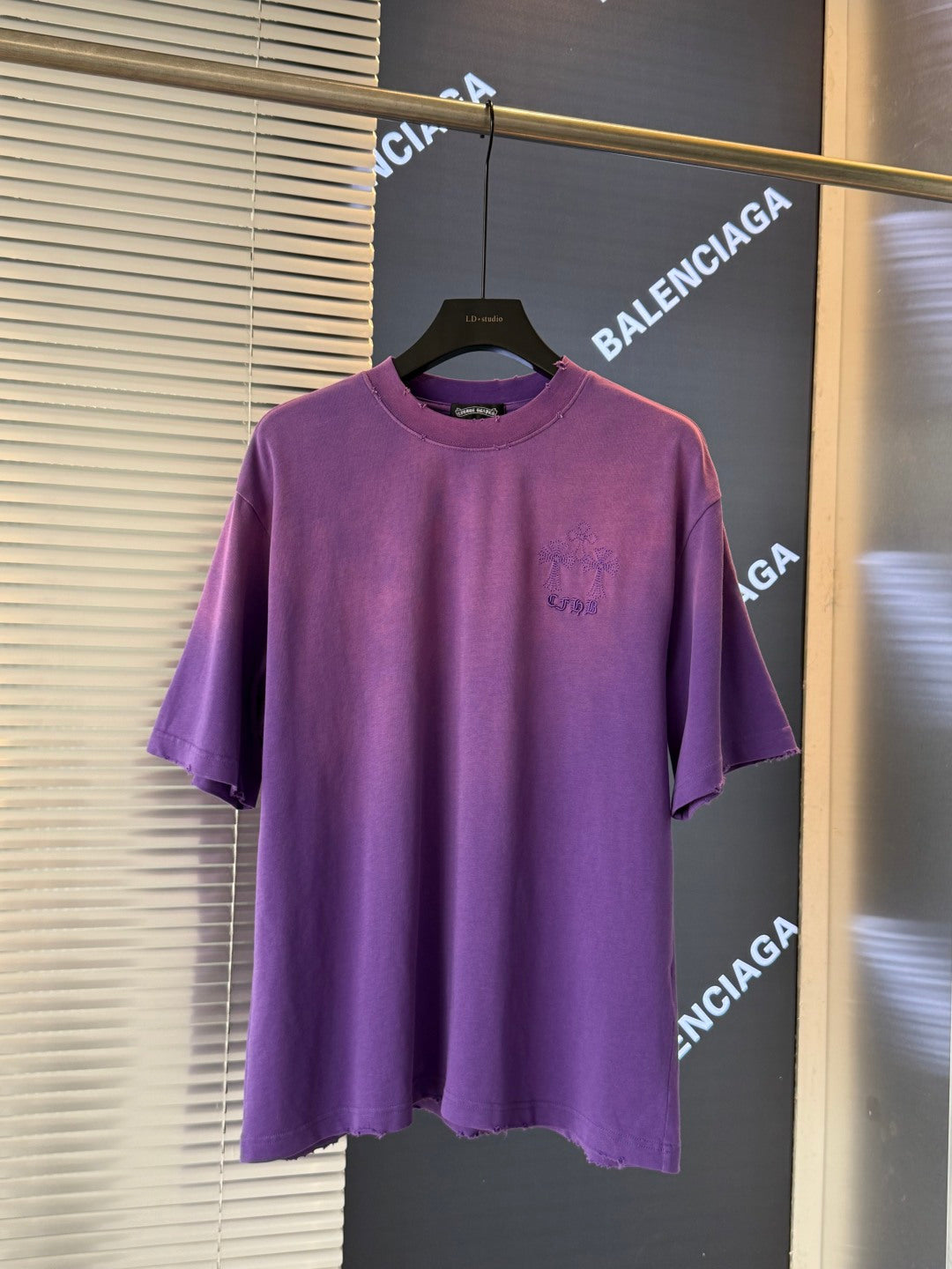 Purple short-sleeve T-shirt on a hanger with a small embroidered chest graphic.