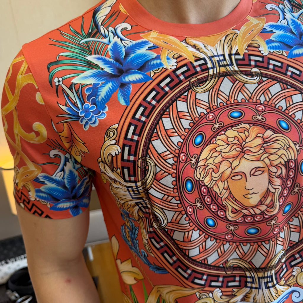 Graphic print T-shirt close-up of blue flowers and Medusa medallion on red-orange