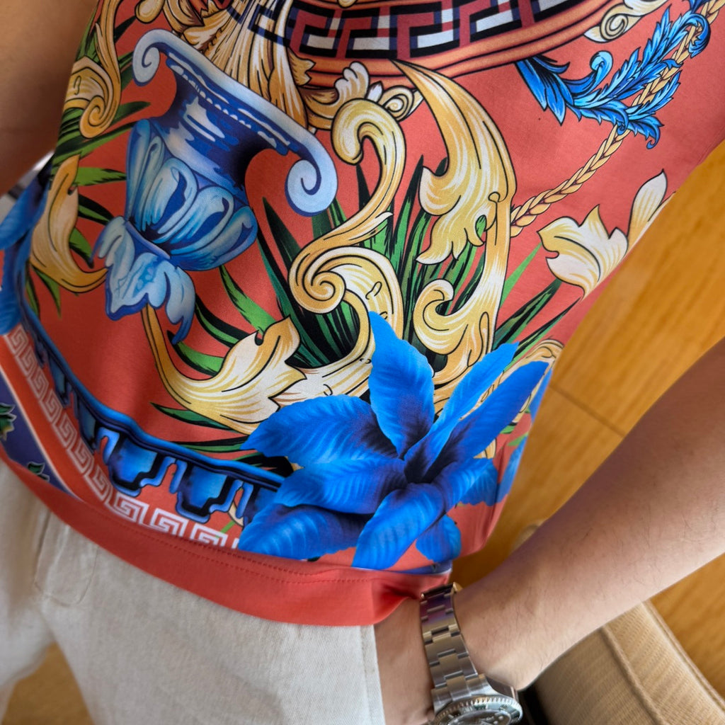 Graphic print T-shirt close-up of ornate scrollwork, blue flowers, red hem band