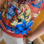 Graphic print T-shirt close-up of ornate scrollwork, blue flowers, red hem band