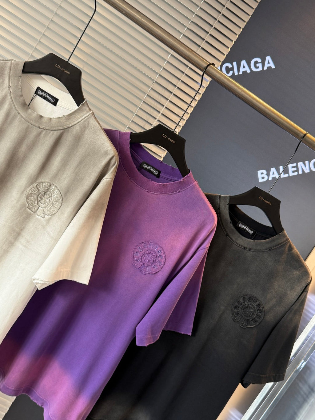 Crewneck short-sleeve T-shirts on hangers in cream, purple, and black with crest prints