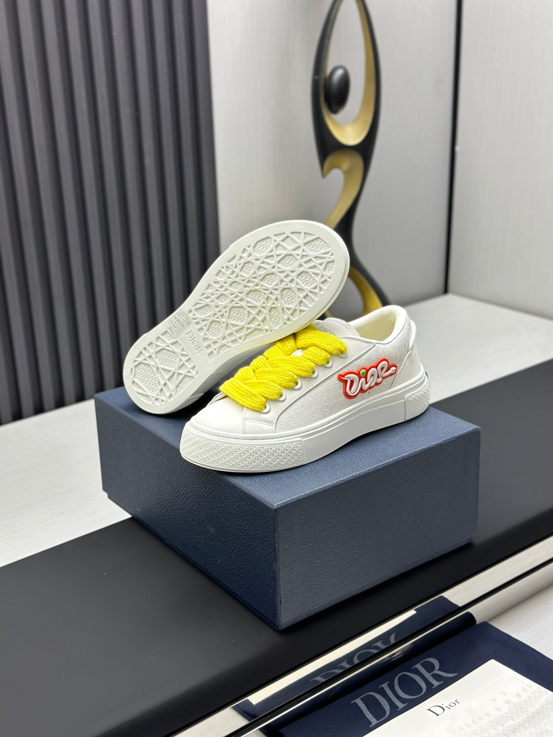 White low-top sneakers with yellow laces, outsole visible on blue shoebox.