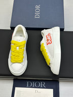 White low-top sneakers with yellow laces, side logo patch visible on blue shoebox.