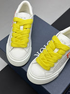 White low-top sneakers with bright yellow laces, top view on blue shoebox.