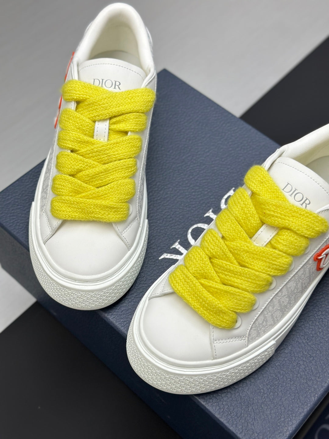 White low-top sneakers with bright yellow laces, top view on blue shoebox.