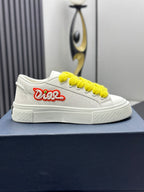 White low-top sneakers with yellow laces and red logo, front view on blue shoebox.