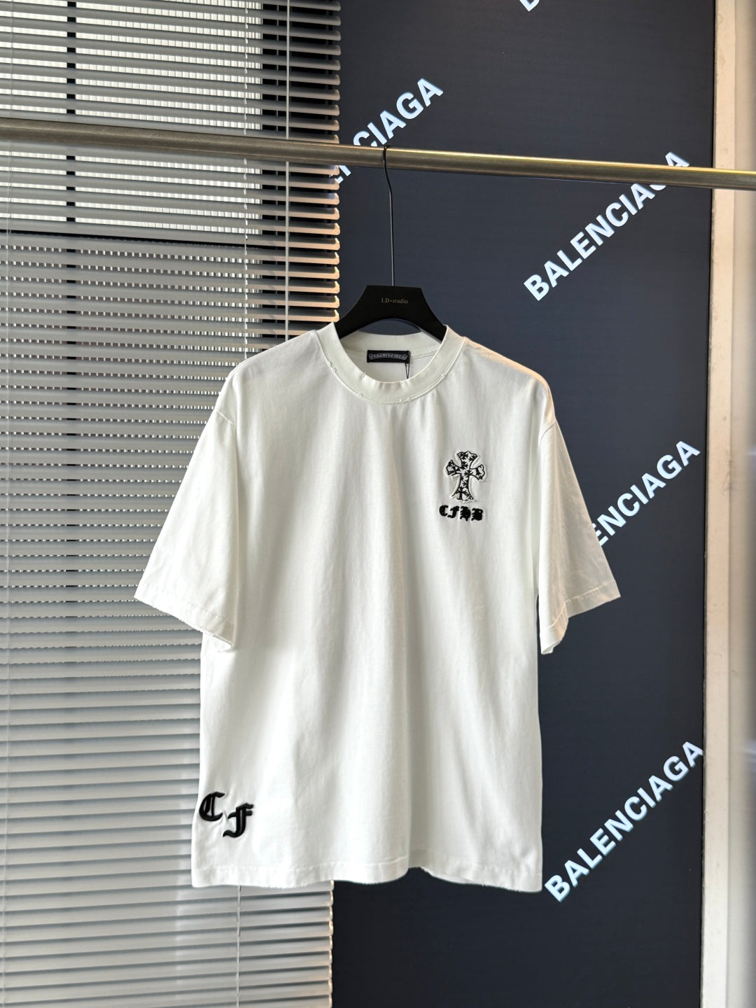 White short-sleeve T-shirt with small black embroidered crest graphic on the chest
