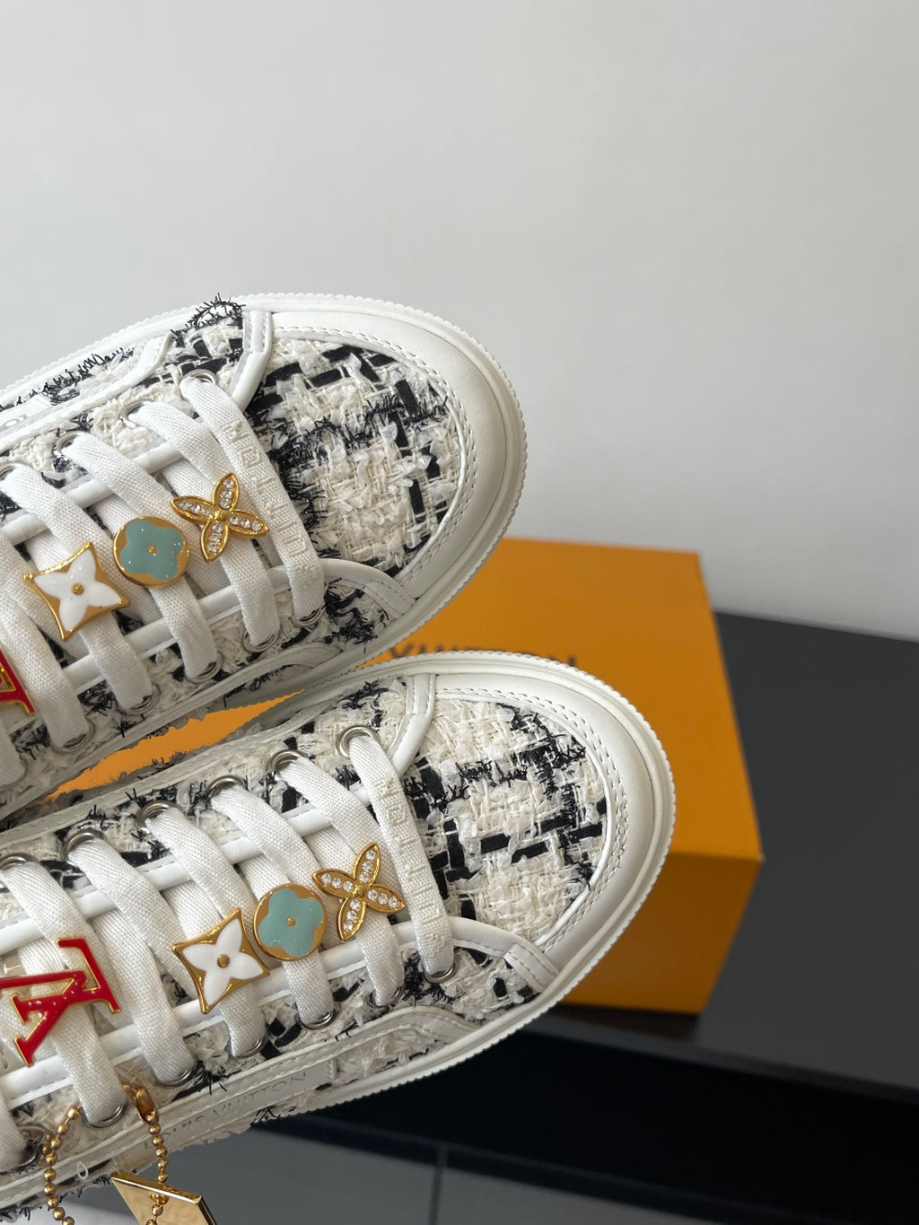 Louis Vuitton women's sneakers close-up, white laces with gold and colored charms.