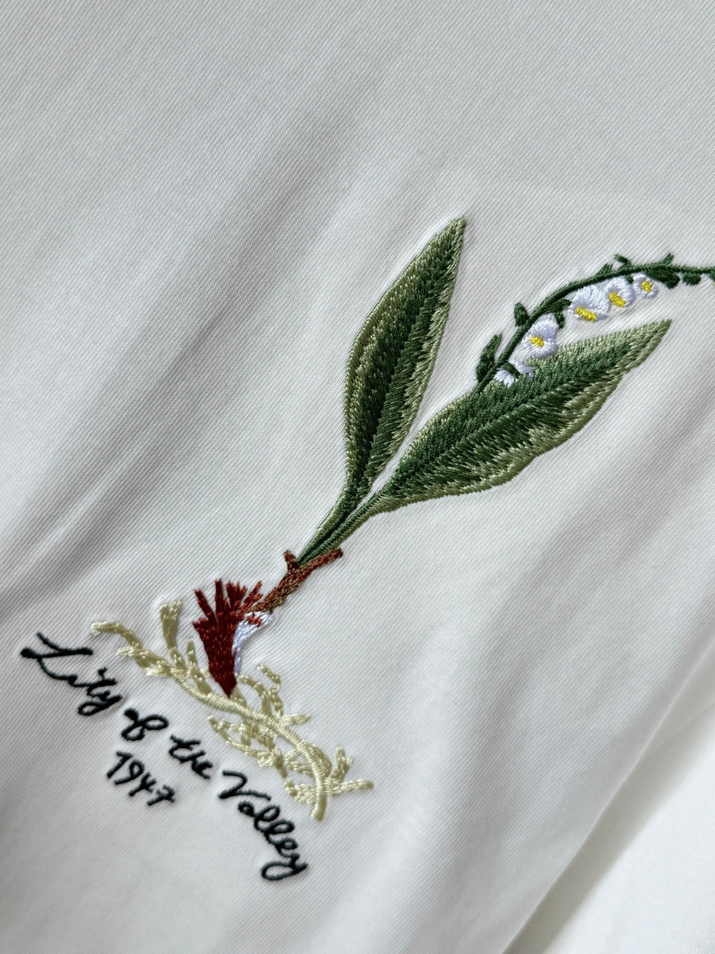 White T-shirt close-up with green leaf and bird embroidery on the chest