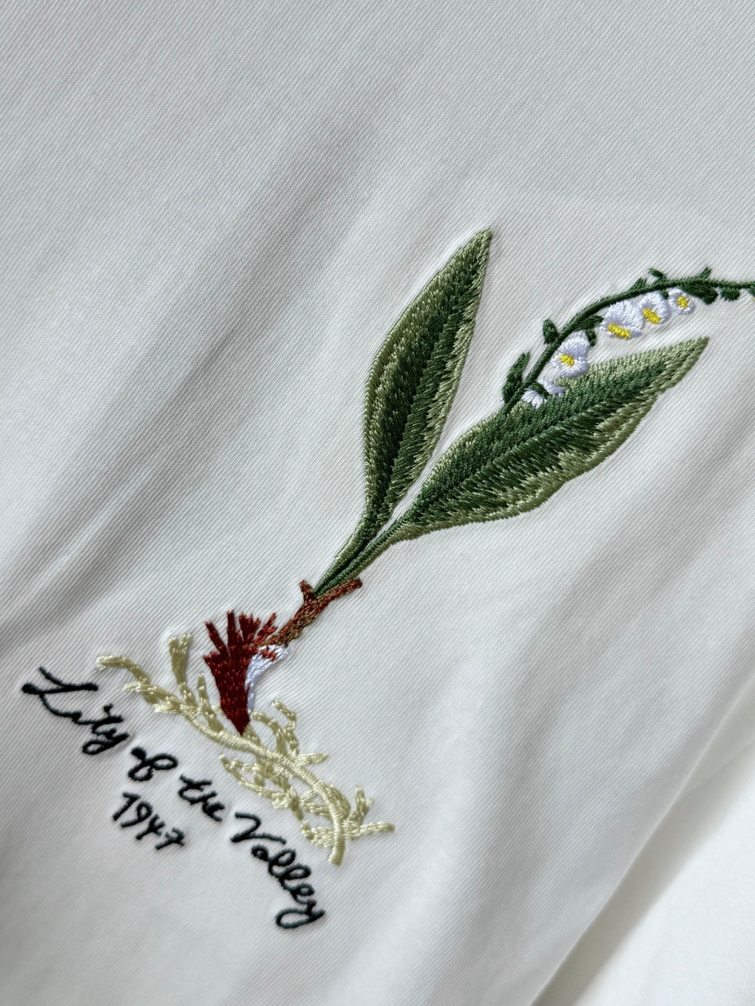 White T-shirt close-up with green leaf and bird embroidery on the chest