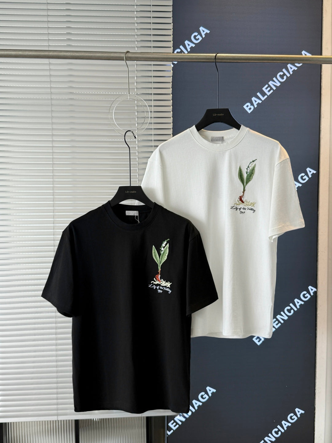 Short-sleeve T-shirts in white and black on hangers, each with chest bird embroidery