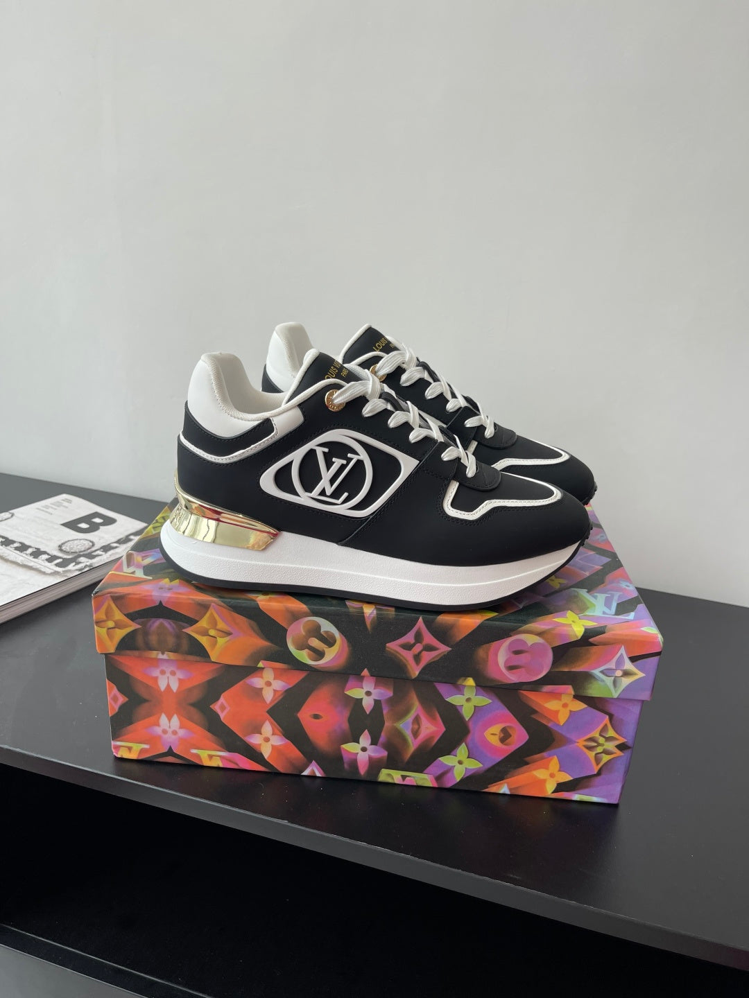 Ladies' Louis Vuitton sneakers on a colorful box, black uppers with white laces and trim.