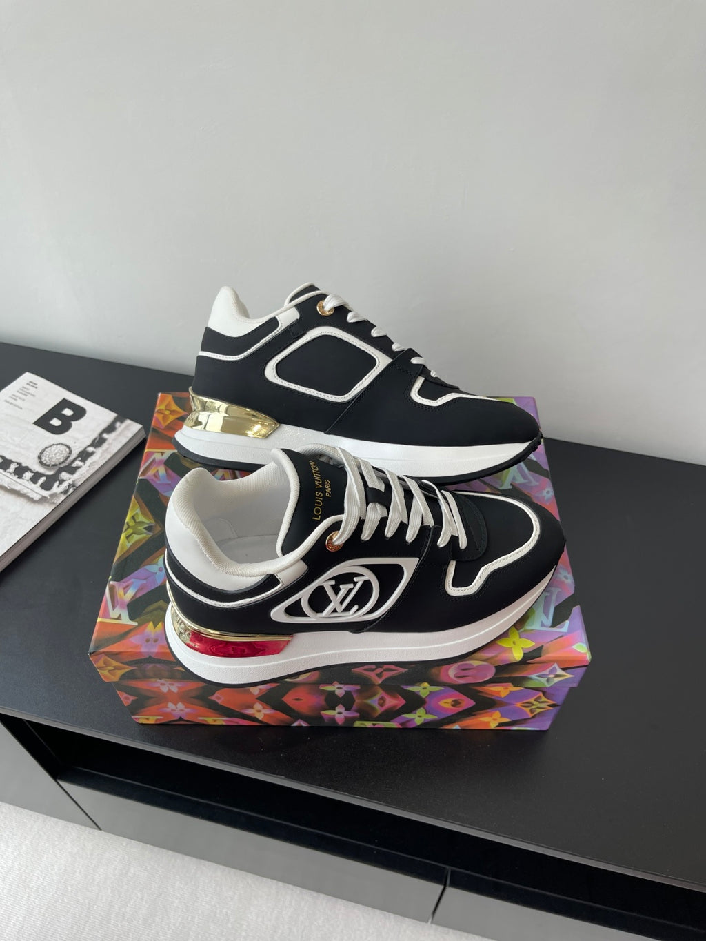 Ladies' Louis Vuitton sneakers angled on box, black uppers with white laces and gold accents.