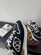 Ladies' Louis Vuitton sneakers side view, black leather look with white piping and gold emblem.